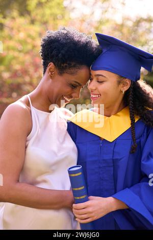 Orgogliosa madre che festeggia con la figlia adolescente che indossa gli abiti per laureati all'aperto Foto Stock