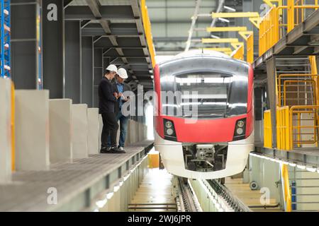 Ritratto completo di due supervisori maschi che utilizzano un tablet digitale per discutere della manutenzione del sistema skytrain elettrico. Poll Foto Stock