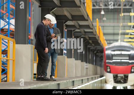 Ritratto completo di due supervisori maschi che utilizzano un tablet digitale per discutere della manutenzione del sistema skytrain elettrico. Poll Foto Stock