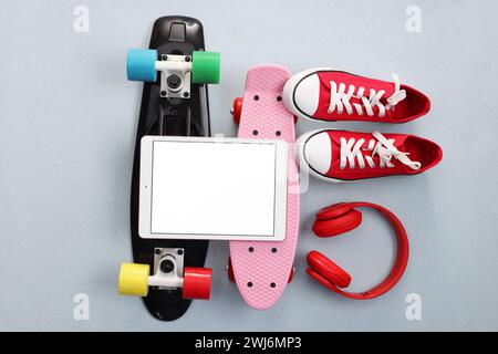 Tablet moderno, cuffie, skateboard e scarpe su sfondo grigio chiaro, piatto. Spazio per il testo Foto Stock