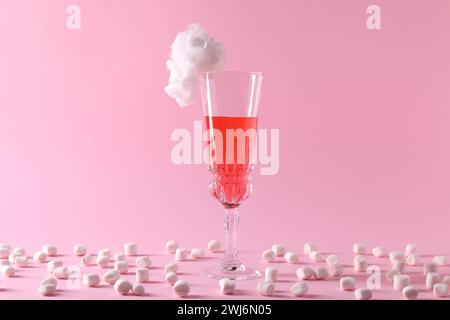 Gustoso cocktail in vetro decorato con caramelle di cotone e marshmallow su sfondo rosa Foto Stock