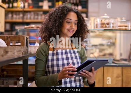 Giovane donna sorridente che indossa il grembiule che lavora in un negozio di alimentari utilizzando un tablet digitale Foto Stock