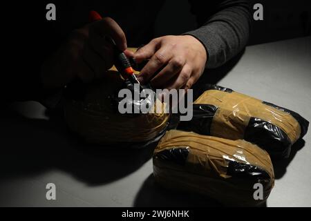 Contrabbando e traffico di droga. Uomo che apre un pacchetto di narcotici con un taglierino nell'oscurità, primo piano Foto Stock