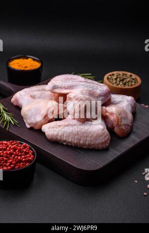 Ali di pollo crude con sale, spezie ed erbe aromatiche su un tagliere di legno Foto Stock