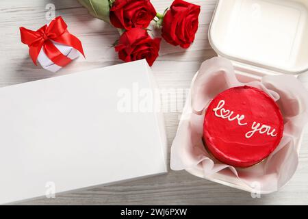 Gustosa torta bento in confezione da asporto, rose e confezione regalo su un tavolo di legno bianco, piatto Foto Stock