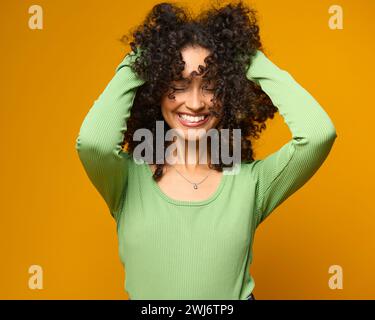 Studio Ritratto di donna sorridente in piedi su sfondo giallo che regge i capelli Foto Stock
