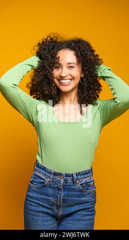 Studio Ritratto di donna sorridente in piedi su sfondo giallo che regge i capelli Foto Stock
