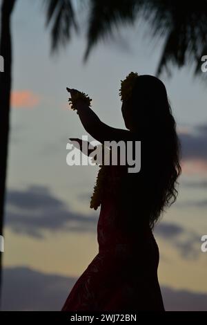 Una giovane ballerina hula si esibisce sulla riva di Waikiki Beach alle Hawaii, mentre il cielo del tramonto la rende in silhouette Foto Stock