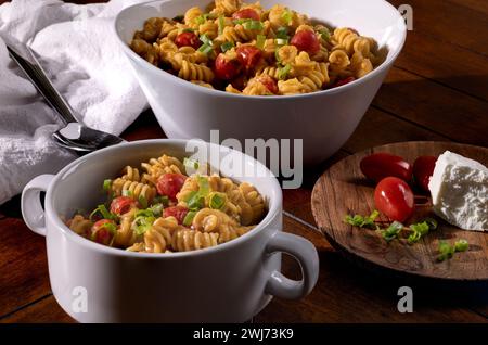 Insalata primaverile di macaroni a spirale con pomodori in un recipiente da portata su un tavolo di legno Foto Stock