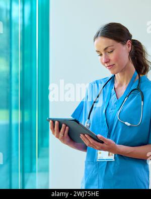 Ritratto del medico donna che indossa scrub che guarda il tablet digitale in ospedale Foto Stock