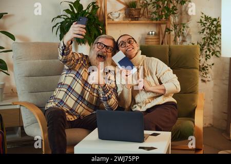 Coppia senior felice ed eccitata, uomo e donna che si fanno selfie, mostrano i biglietti e conoscono gli amici sul prossimo viaggio Foto Stock