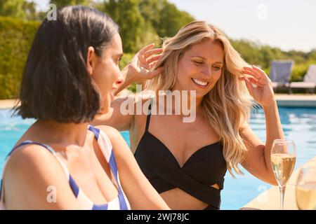 Due amiche mature che indossano costumi da bagno all'aperto in piscina bevendo champagne il giorno della Spa Foto Stock