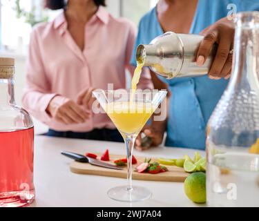 Primo piano di amiche a casa che si divertono a versare cocktail in Glass insieme Foto Stock