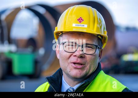 13 febbraio 2024, Meclemburgo-Pomerania occidentale, Rostock: Carsten Schneider, Commissario del governo federale per la Germania orientale, risponde alle domande dei rappresentanti dei media di fronte a enormi tubi metallici per le fondamenta di turbine eoliche offshore presso l'impianto di tubi speciali EEW nel porto marittimo. L'azienda produce fondazioni per turbine eoliche offshore e trasforma l'acciaio spessa in tubi con diametro fino a 10 metri. Politici, tra cui il Commissario del governo federale per l'Europa orientale, Schneider e i sindacalisti visitano Wind turbin Foto Stock