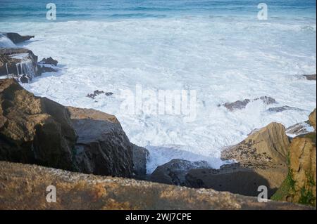 Sfondo naturale di onde che si infrangono sulla costa, creando schiuma bianca mentre si rompe su una spiaggia rocciosa. Un incredibile potere di onde che si infrangono su rocce pericolose. SL Foto Stock