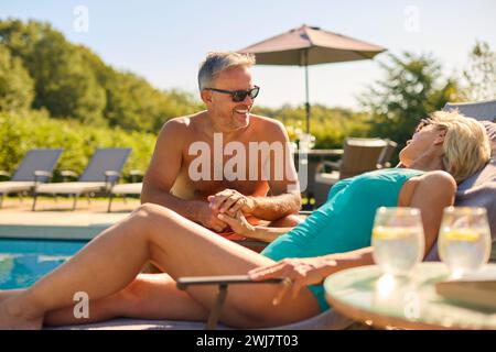 Coppia senior in vacanza con costumi da bagno che si rilassano presso la piscina dell'hotel Foto Stock