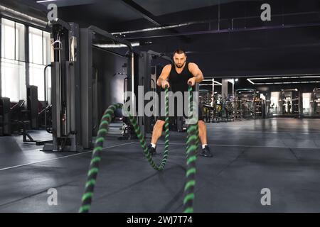 Allenamento CrossFit. Uomo muscoloso motivato che si allena con le corde da battaglia in palestra Foto Stock