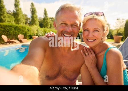 Foto POV della coppia senior in vacanza in posa per Selfie con costumi da bagno presso la piscina Foto Stock