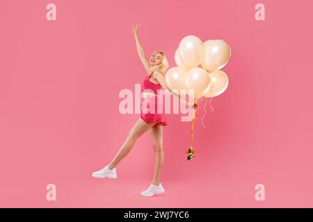 Giovane donna felice che balla con palloncini in costume corallino Foto Stock