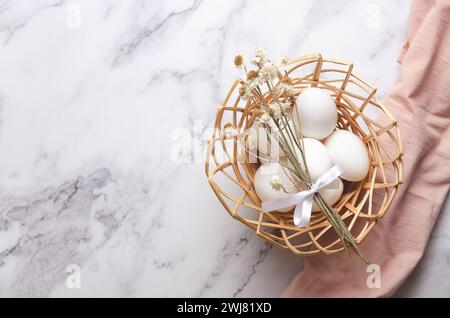 Uova di Pasqua in un cestino su sfondo di marmo bianco con tovagliolo rosa e spazio per le copie. Foto Stock