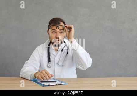 Scioccato medico terapeuta di mezza età si toglie gli occhiali e guarda la macchina fotografica Foto Stock