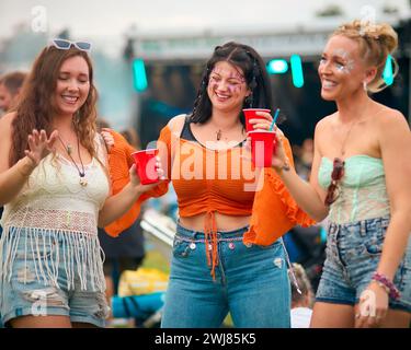 Tre amiche che indossano balli scintillanti al Summer Music Festival e tengono un drink Foto Stock