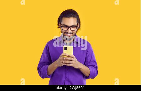 Giovane appassionato uomo del Sud asiatico blogger che tiene il telefono cellulare in piedi in uno studio giallo Foto Stock
