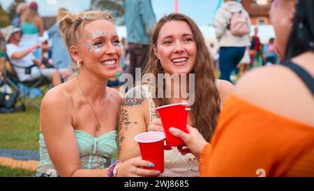 Tre amiche che indossano Glitter Having Fun al Summer Music Festival che tengono un drink Foto Stock