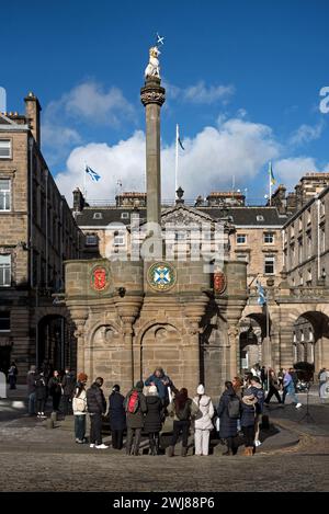 I turisti in un tour a piedi si riuniscono alla Mercat Cross di fronte alle City Chambers sulla High Street nella città vecchia di Edimburgo. Foto Stock