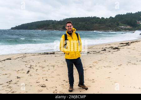 Ritratto di un uomo con una giacca gialla che sorride su una spiaggia di sabbia bianca Foto Stock