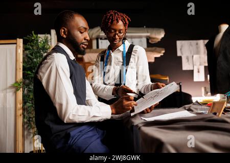 Brainstorming apprendisti sarti che guardano i disegni di una collezione su misura immaginata da un maestro stilista. Colleghi dell'atelier di lavoro di squadra che discutono degli adeguamenti sartoriali da apportare Foto Stock