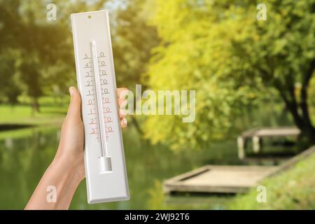 Donna che tiene il termometro nel parco nelle giornate di sole, primo piano Foto Stock