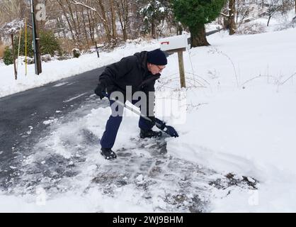 Chappaqua, New York - 13 febbraio 2024 - Un uomo esce dal vialetto dopo una tempesta invernale scaricata su un piede di neve pesante e bagnata nella contea di Westchester, New Yo Foto Stock