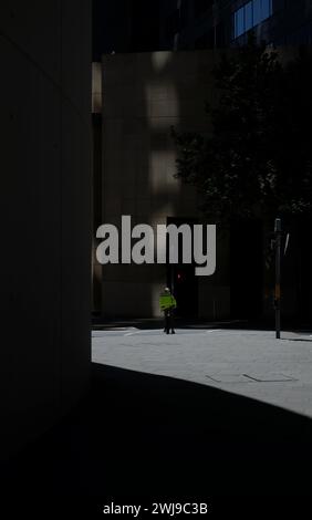 Un corriere di consegna del cibo in un bagno di luce solare tra le ombre profonde nel CBD di Sydney Foto Stock