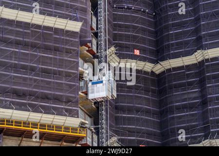 Vista su un edificio in costruzione realizzato con ponteggi in cemento e ascensore per i lavoratori Foto Stock