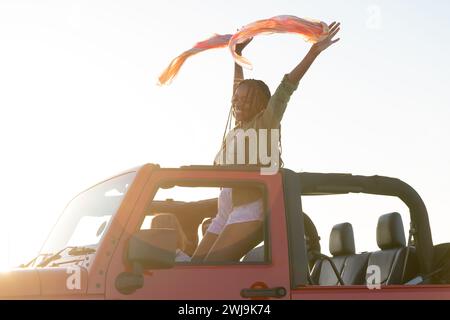 La giovane donna afroamericana gode di un tramonto vibrante da un veicolo durante un viaggio in auto Foto Stock