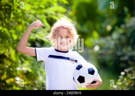 I bambini giocano a football all'aperto. Tifosi della Germania con bandiera nazionale. I bambini segnano un gol alla partita di calcio. Bambino in maglia tedesca Foto Stock