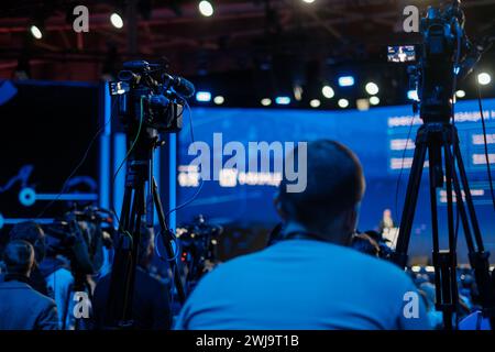 Produzione video in azione in un evento live: Le telecamere catturano un relatore pubblico sul palco con il pubblico in primo piano. Foto Stock