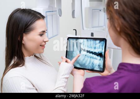 Dentista che mostra al paziente l'immagine radiografica dei denti della mascella presso lo studio dentistico. Foto Stock