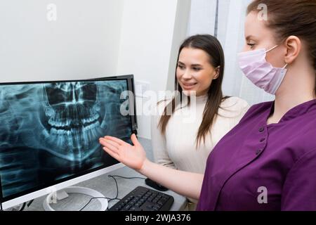 Il dentista mostra i raggi X dei denti sullo schermo al paziente nella clinica. Foto Stock