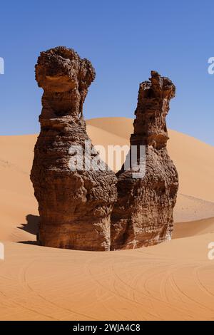 Due torreggianti formazioni di arenaria, simili a sculture naturali, si innalzano sopra le lisce dune del deserto sotto un cielo azzurro Foto Stock