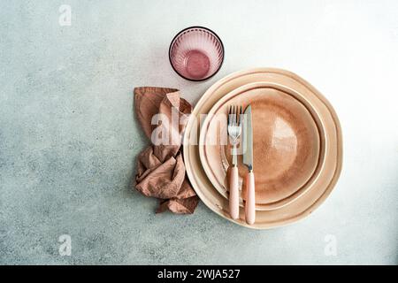 Dall'alto sofisticato tavolo pasquale con piatti in ceramica impilati, posate in oro rosa e tovagliolo di lino su sfondo testurizzato. Foto Stock