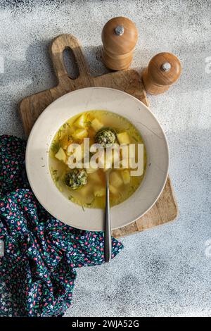 Dall'alto della ciotola di saporita zuppa di polpette con verdure a dadini, presentata su un tagliere rustico in legno, abbinata a un tovagliolo a motivi geometrici e stagionatura Foto Stock