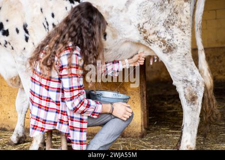 Giovane contadina che munge manualmente una mucca da latte. Benessere e cura degli animali in un'azienda agricola biologica. Foto Stock