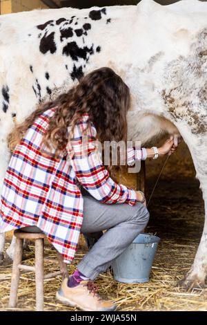 Giovane contadina che munge manualmente una mucca da latte. Benessere e cura degli animali in un'azienda agricola biologica. Foto Stock