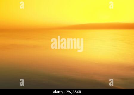 Tramonto dorato astratto sull'acqua tranquilla con onde morbide e orizzonte luminoso. Foto Stock