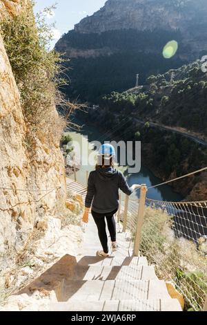 Escursionista anonimo che scende una scala sul sentiero del Caminito del Rey con un fiume e montagne sullo sfondo Foto Stock