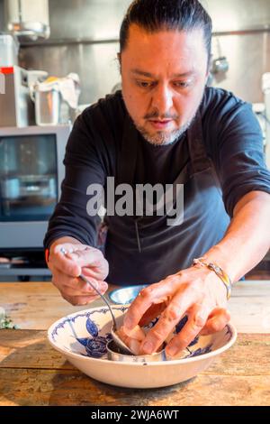 Cuoco con barba positiva in grembiule che usa il cucchiaio per servire deliziosi filetti di pesce a fette al ristorante Zermatt Switzerland Foto Stock