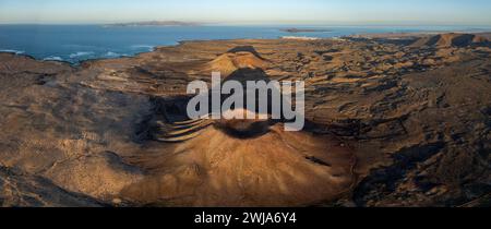 L'immagine aerea cattura un vasto paesaggio vulcanico bagnato dalla calda luce del tramonto, con terreno accidentato e ampie vedute della costa Foto Stock
