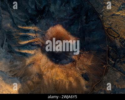 Scatto aereo che cattura l'aspra bellezza di un cratere vulcanico con le sue texture uniche e i colori terrosi, ambientato in un vasto e sereno paesaggio Foto Stock